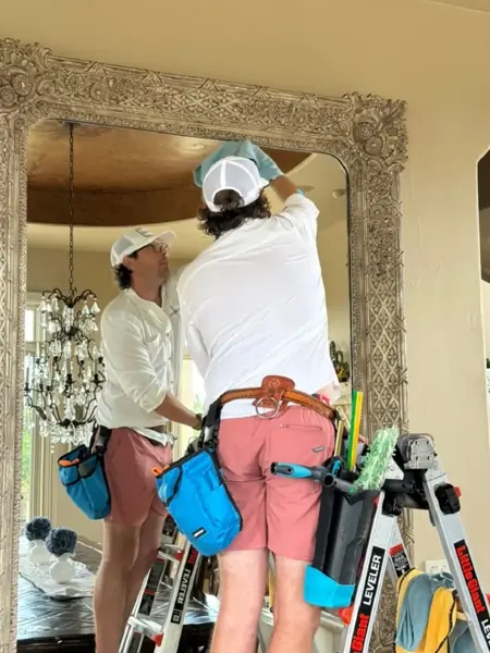 Two Squeaky Clean crew members cleaning a large ornate interior mirror