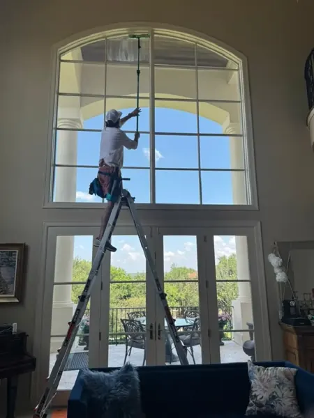 Squeaky Clean technician on a ladder cleaning a tall arched window with an extension pole