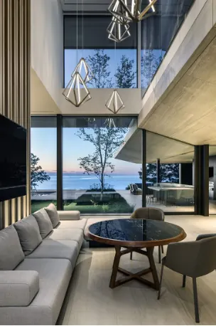 Two-story living room with tall glass walls facing the water at dusk