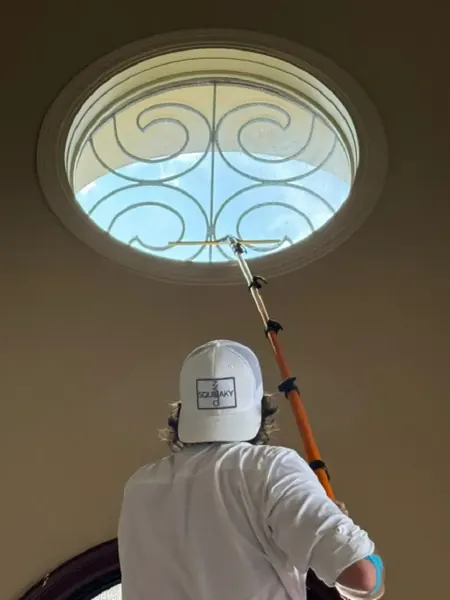 Technician in a Squeaky Clean cap cleaning a round decorative window with an extension pole