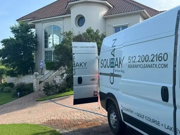 Squeaky Clean van parked at a stone home while a technician cleans exterior windows